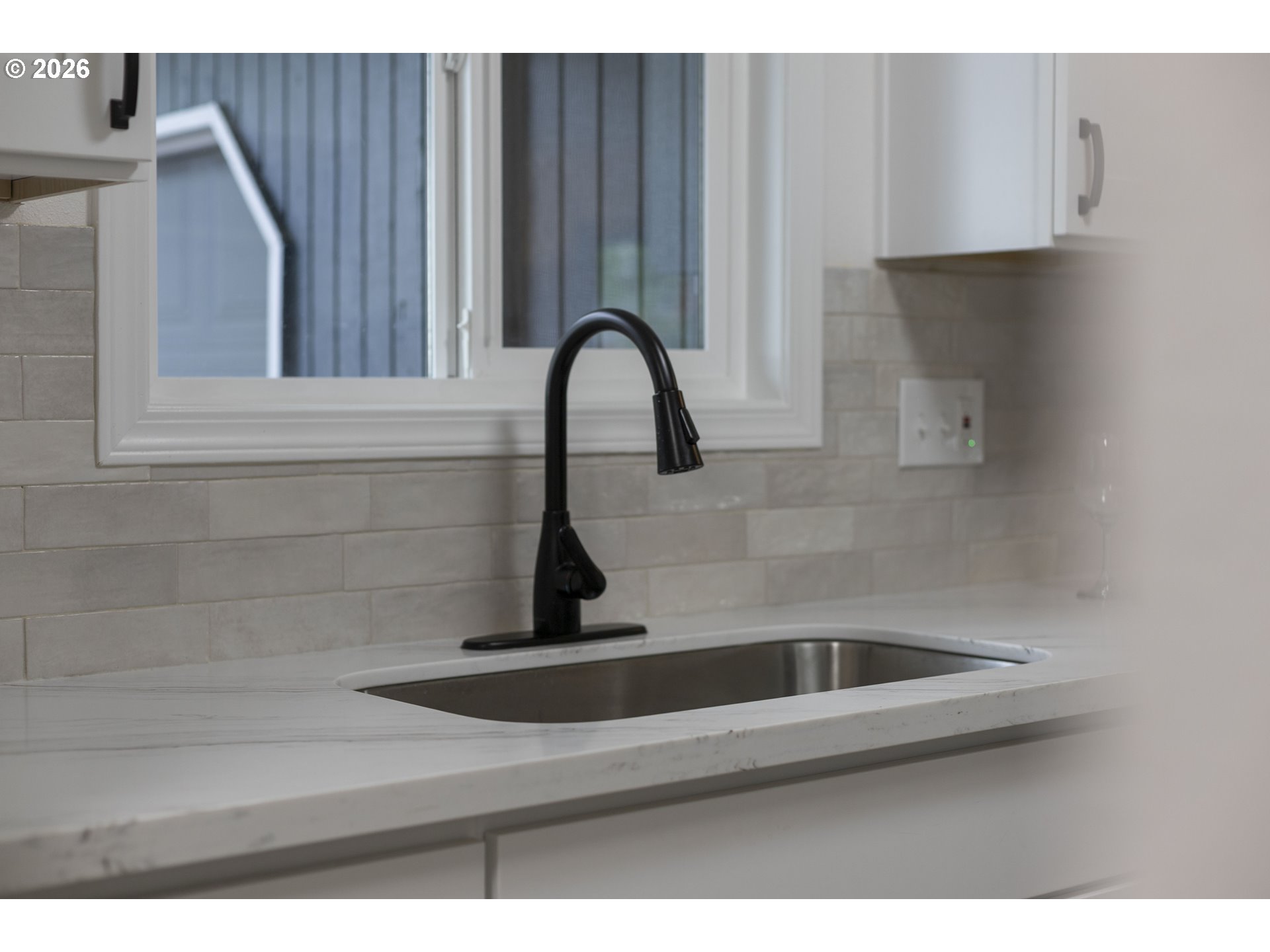 Kitchen sink with a black gooseneck faucet beneath a window, set in a white countertop.