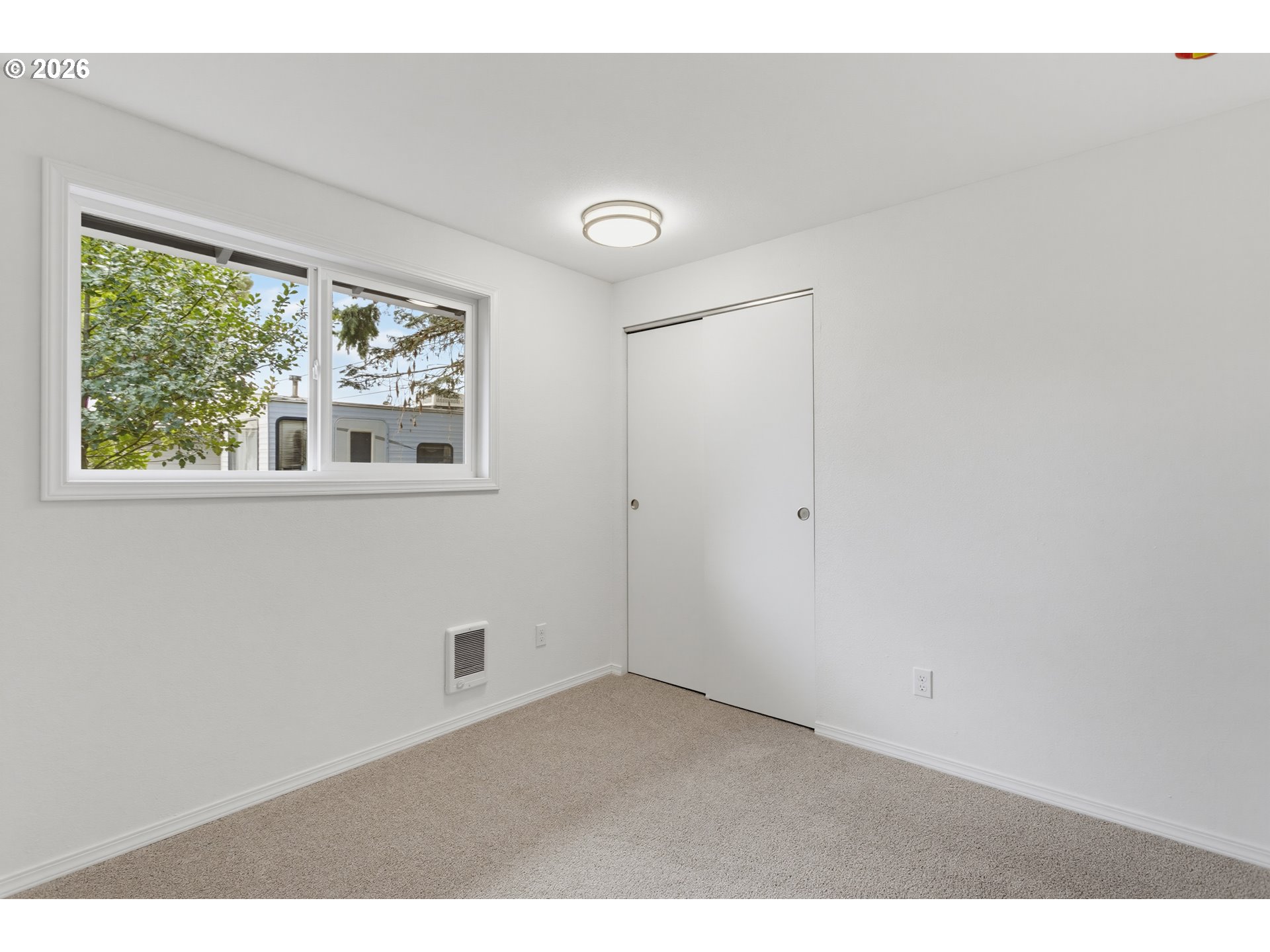 Vacant bedroom with beige carpet, a wide window, and a sliding closet door.