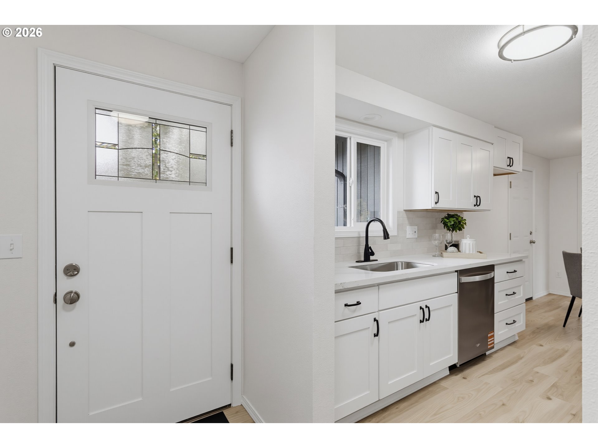 White kitchen with shaker cabinets and stainless-steel dishwasher beside an entry door with decorative glass.