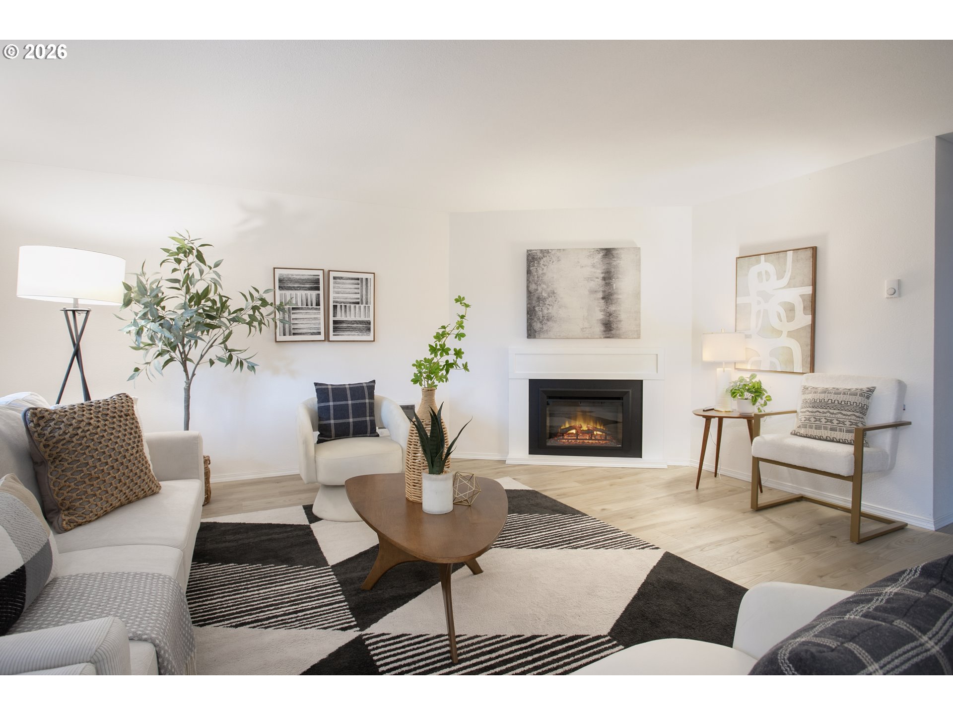 Staged living room with a lit fireplace, white seating, and a bold geometric rug.