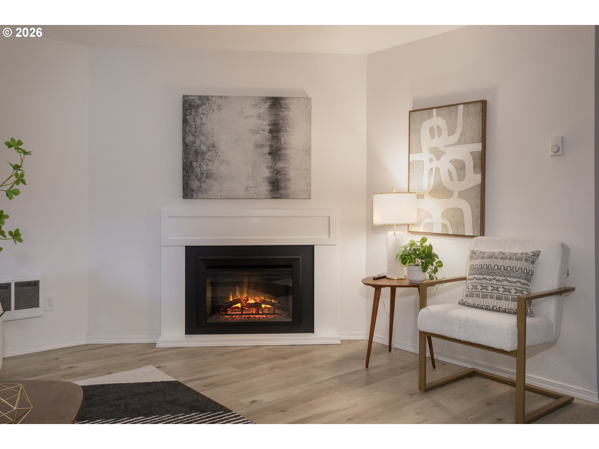 Staged living room with a lit fireplace, white armchair, and abstract wall art.