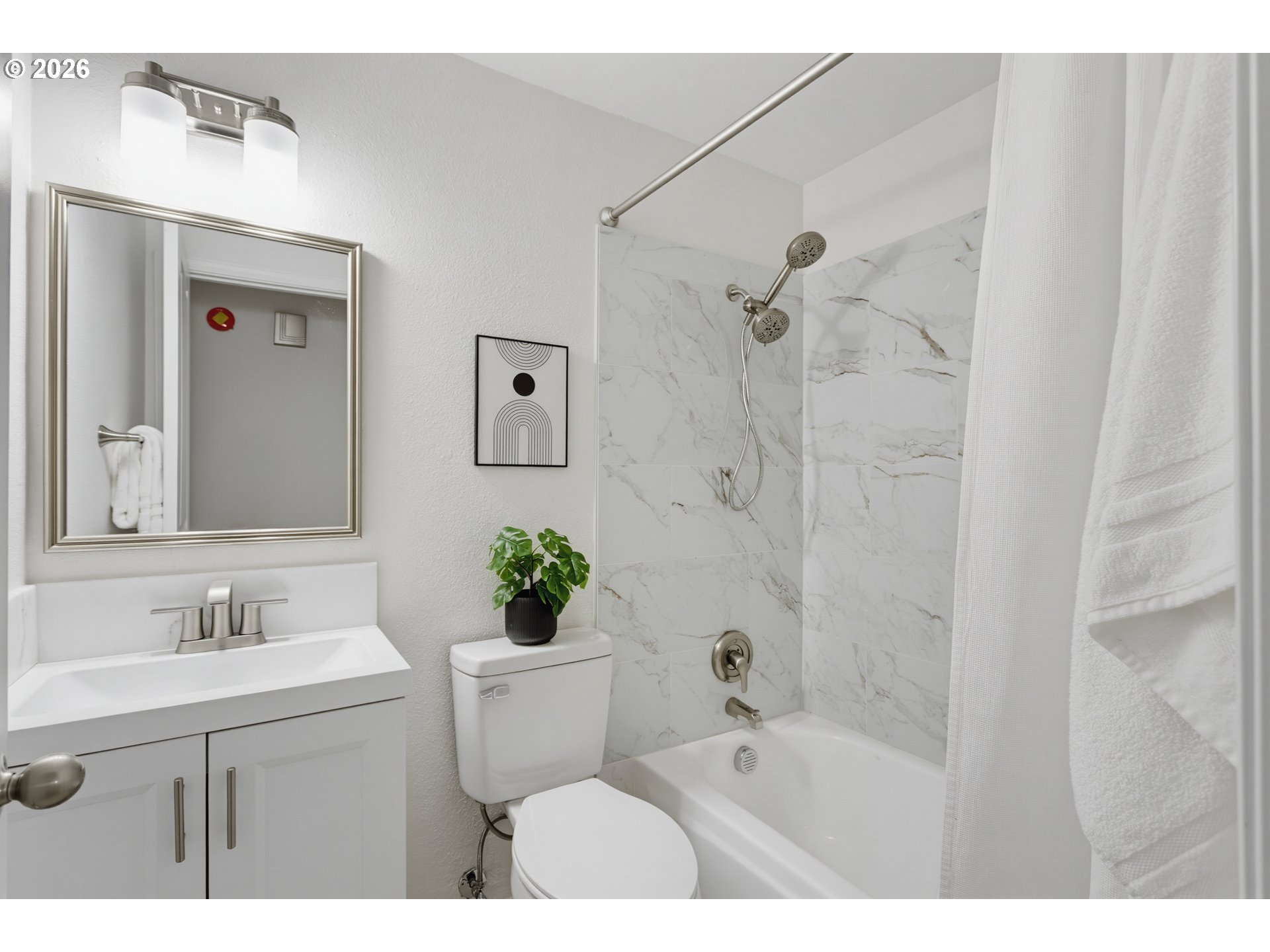 Bathroom with a white vanity and marble-look tub surround with dual showerheads.