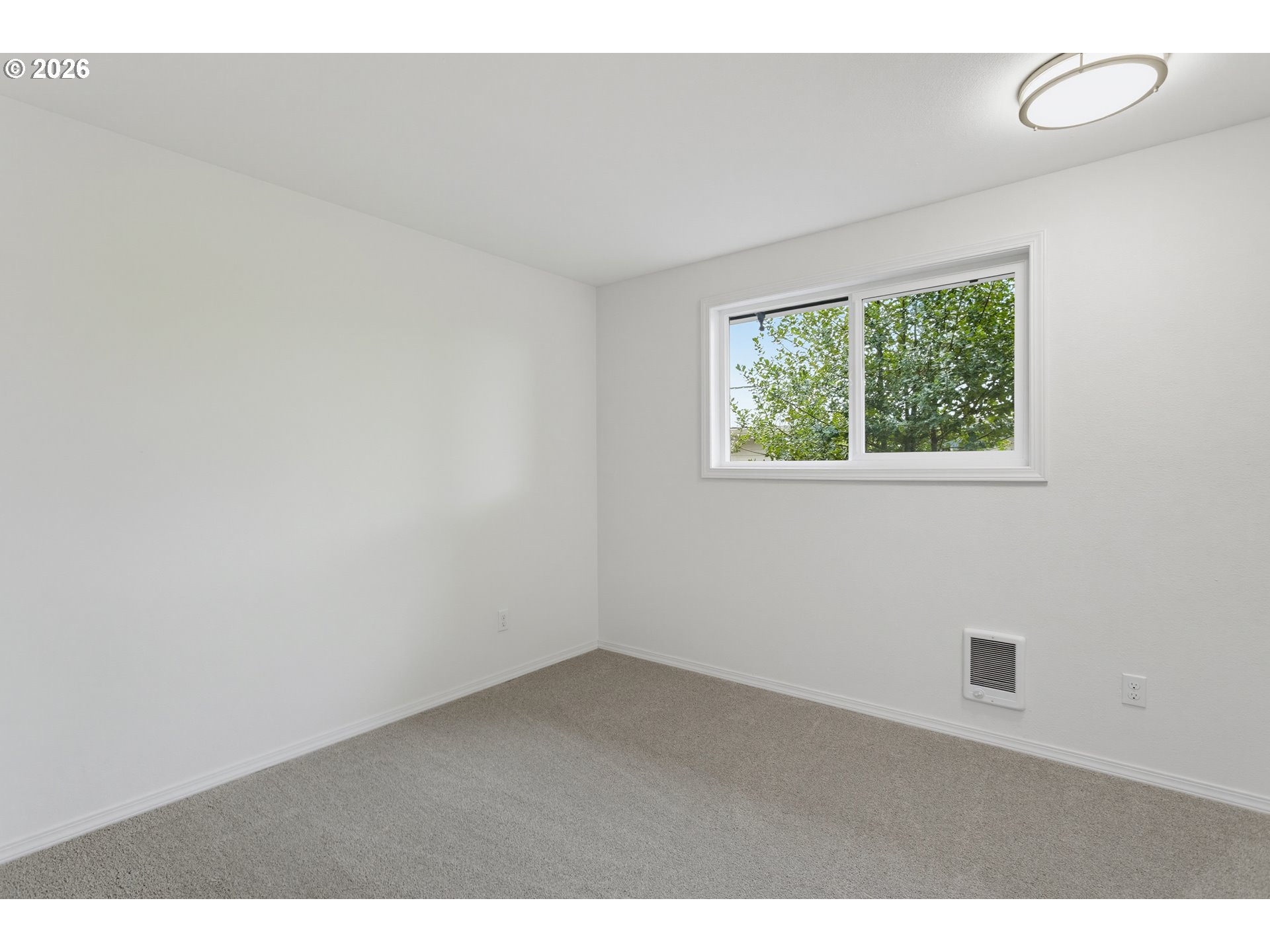 Empty carpeted room with white walls, a wide window, and a wall heater.