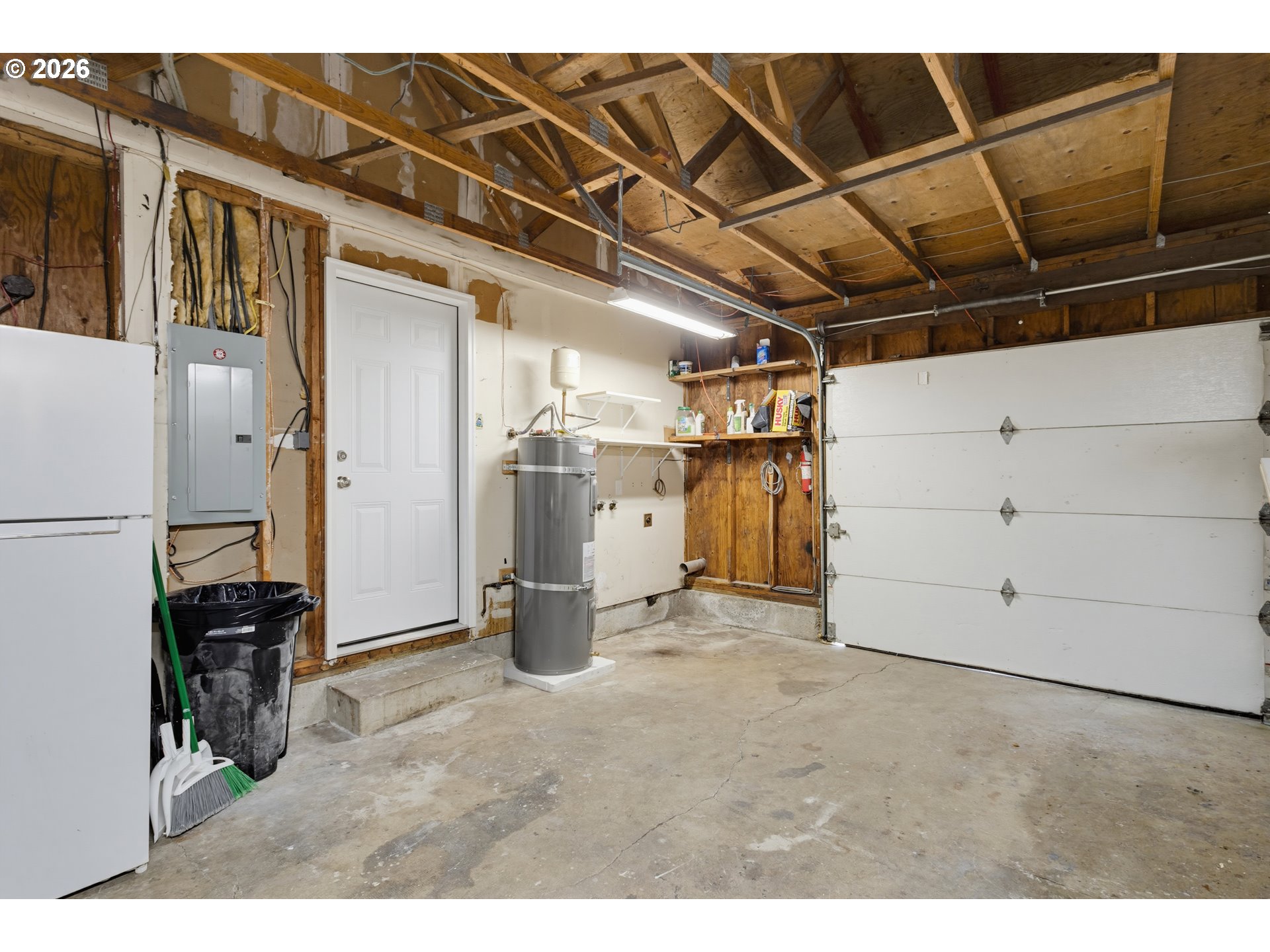Garage with exposed roof framing, a white overhead door, water heater, and concrete floor.