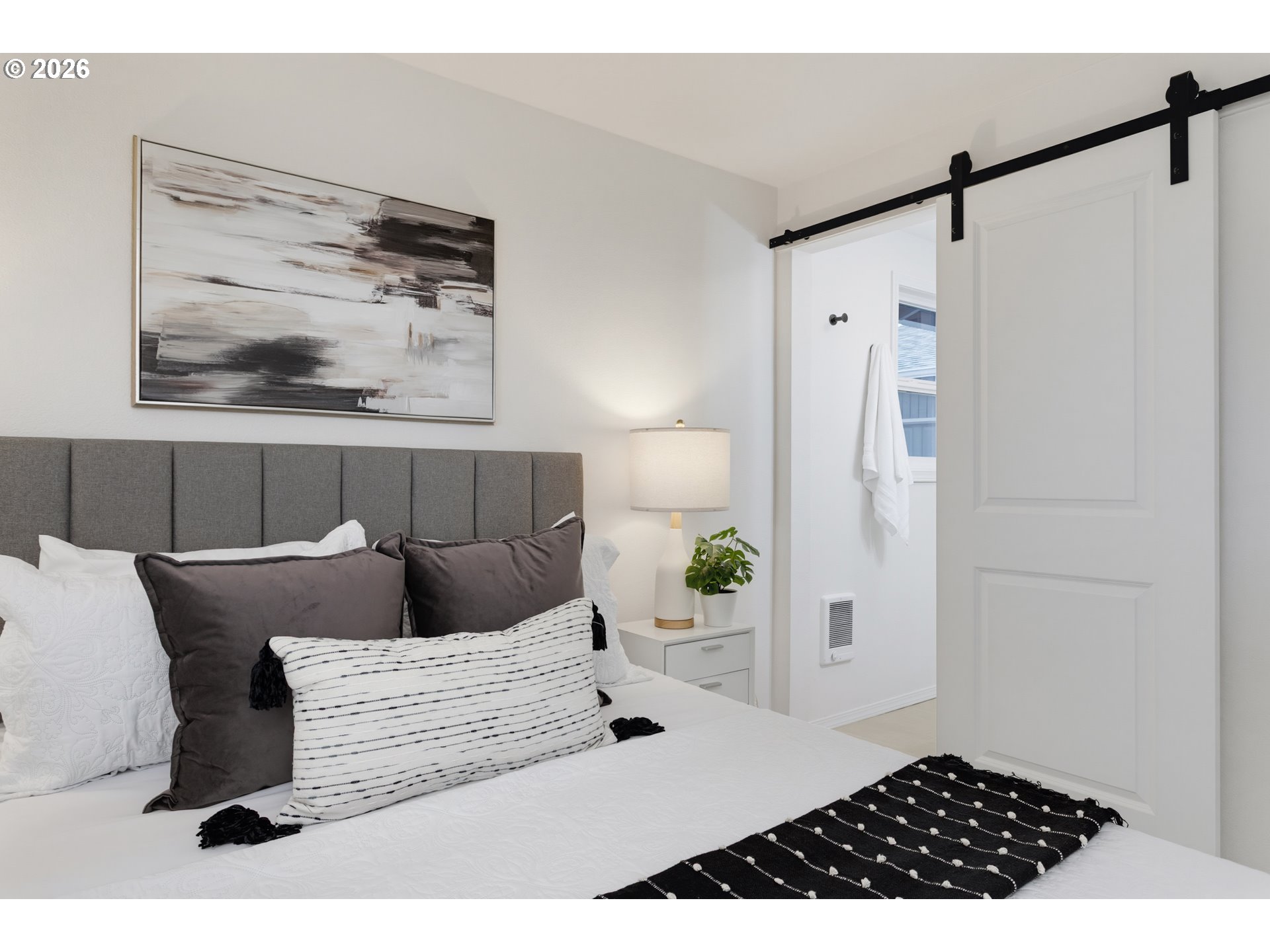 Staged bedroom with a gray upholstered headboard, layered pillows, and a white sliding barn door.