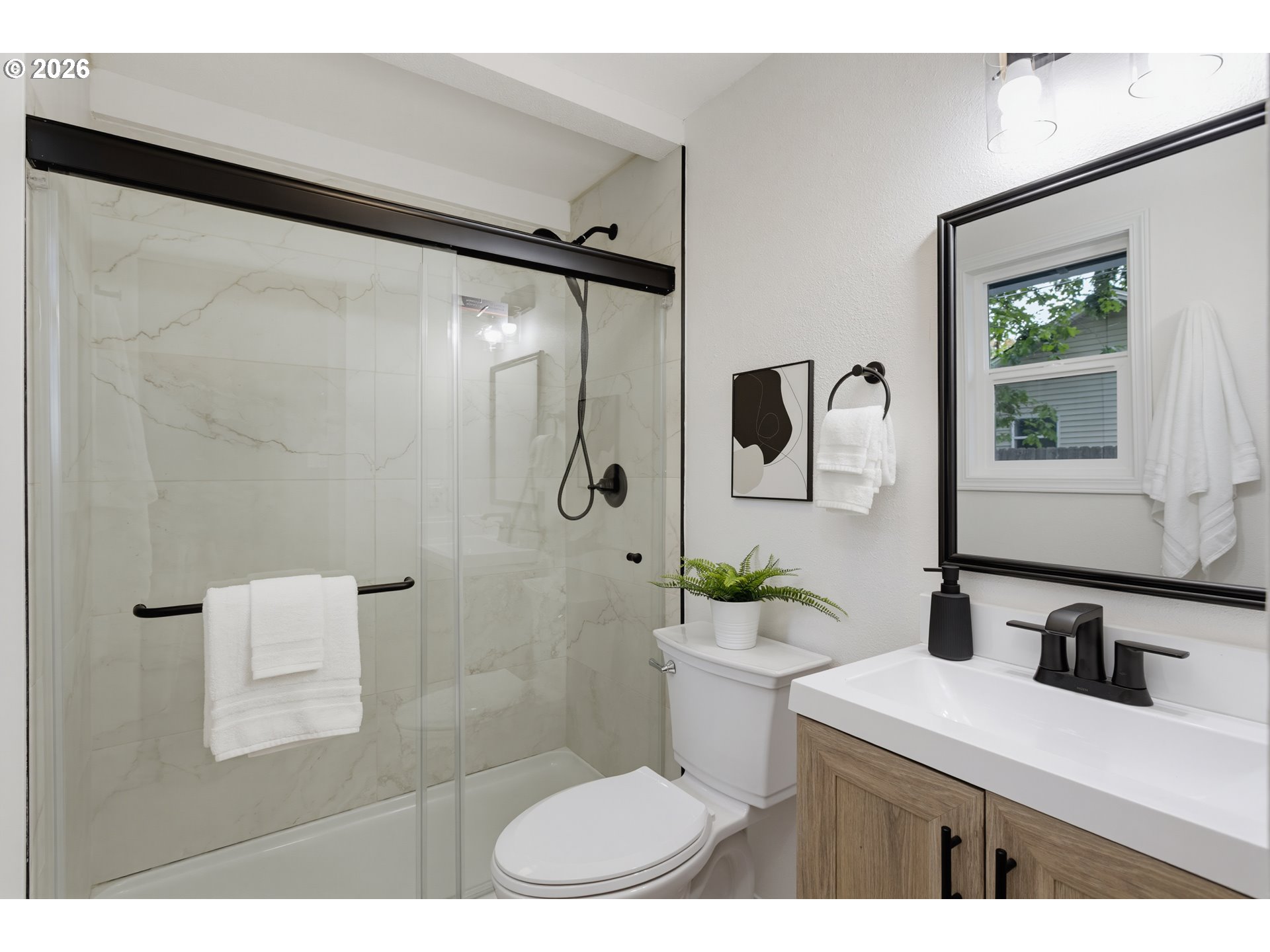 Bathroom with a marble-look tiled glass shower, matte-black fixtures, and a wood-front vanity.
