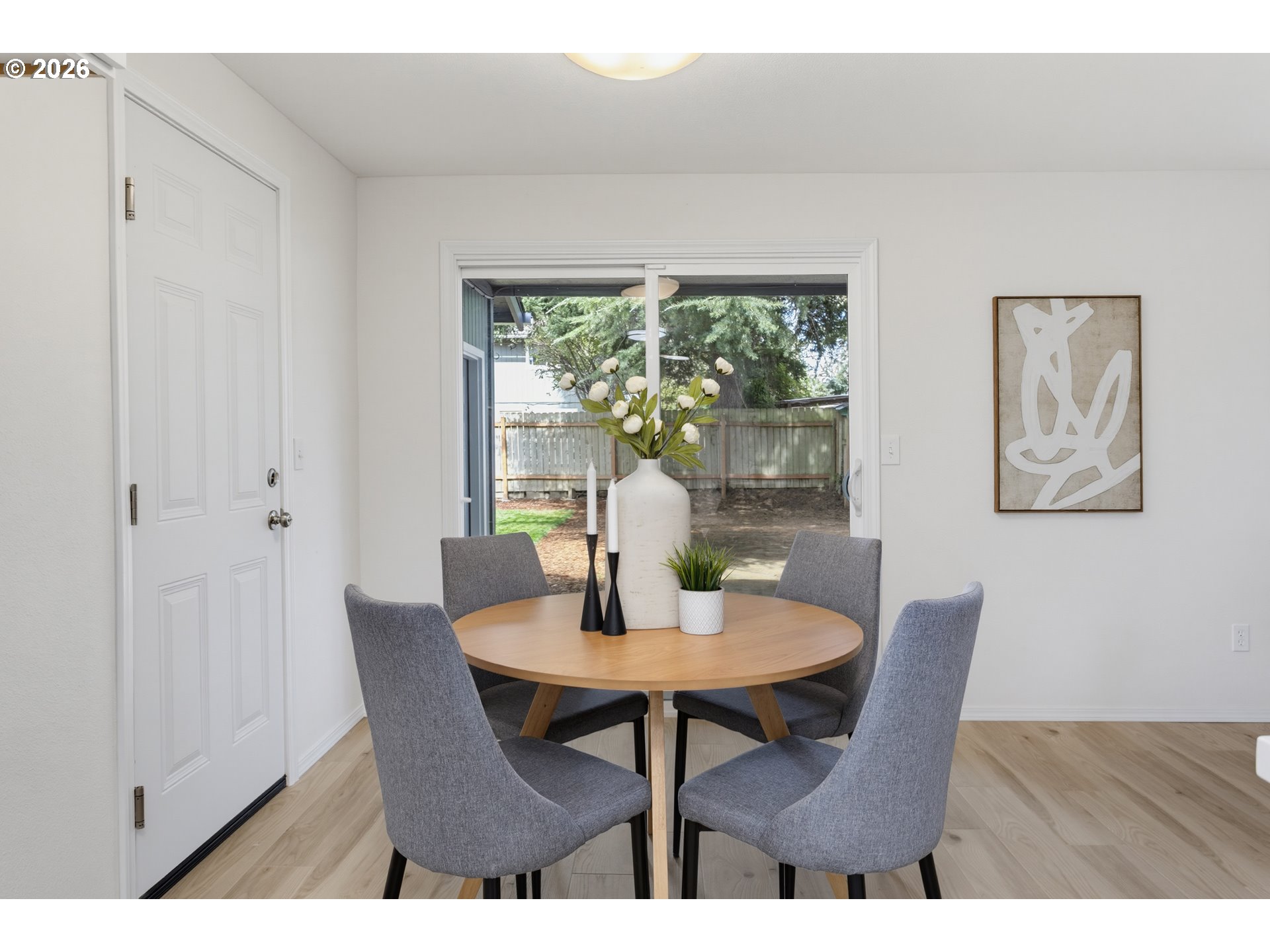 Staged dining area with a round wood table and gray chairs beside a sliding glass door to the backyard.