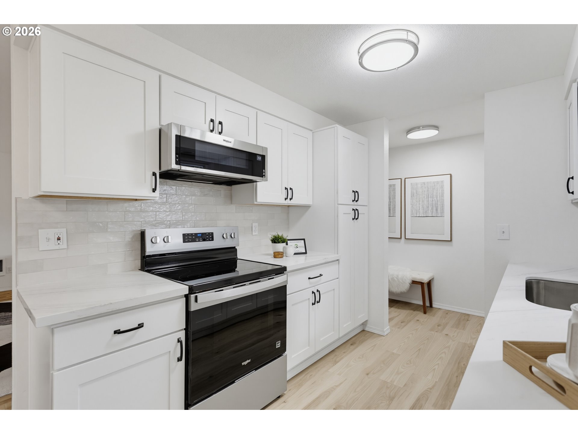 Bright white kitchen with shaker cabinets, stainless appliances, and a white island with sink.