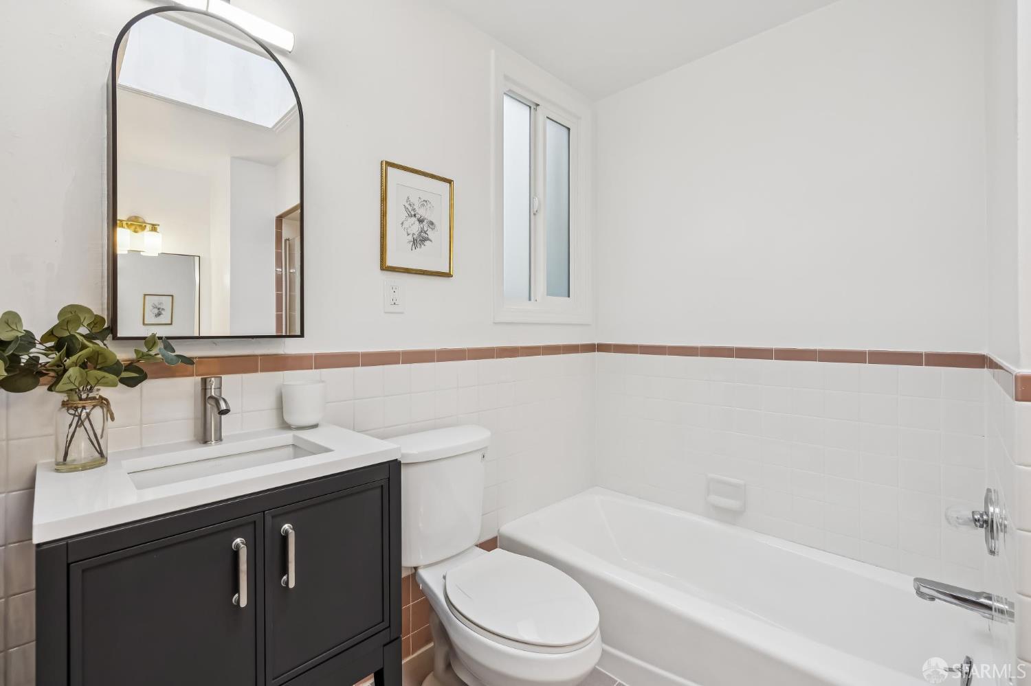 Bright bathroom with a dark vanity, white bathtub, tiled walls, and narrow window.