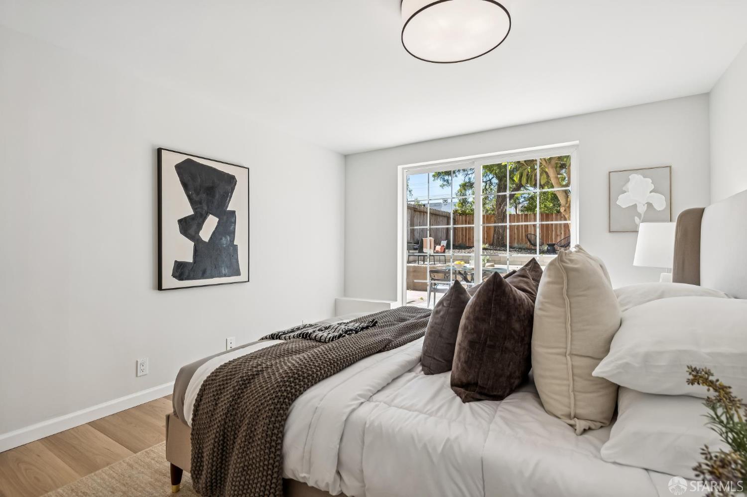 Staged bedroom with a white bed, dark pillows, and sliding glass doors to a fenced backyard.