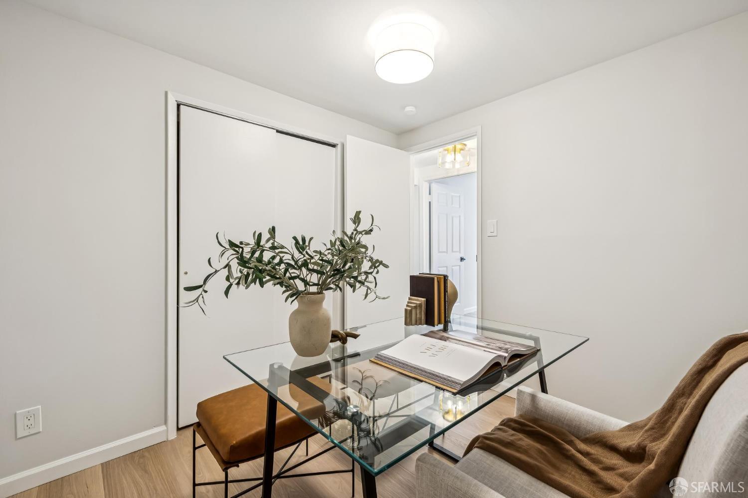 Staged home office with a glass desk, decorative branches, and sliding closet doors.