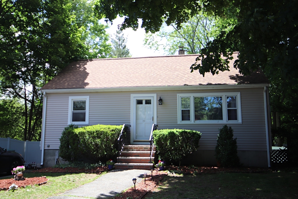 Single-story house with a brown shingle roof, brick entrance steps, and mature trees.