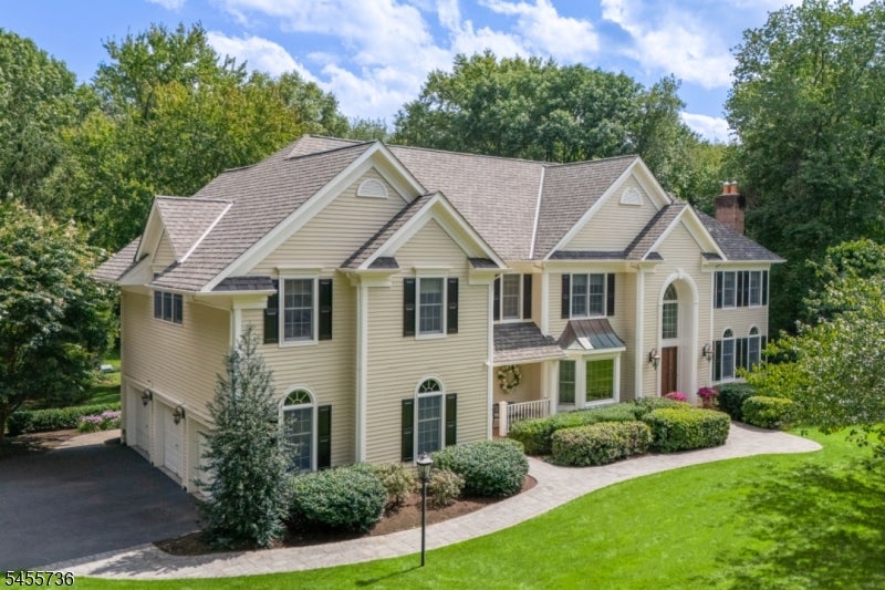Large beige two-story home with multiple gables, an arched entry, landscaped shrubs, and a curved walkway.