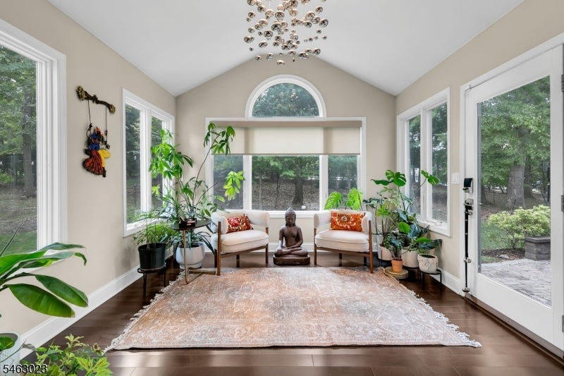 Sunroom with vaulted ceiling, arched window, wooded views, potted plants, and two chairs.