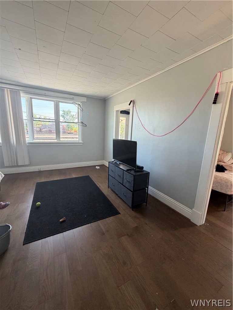 Living room with a large window, dark wood flooring, and a television on a black dresser.