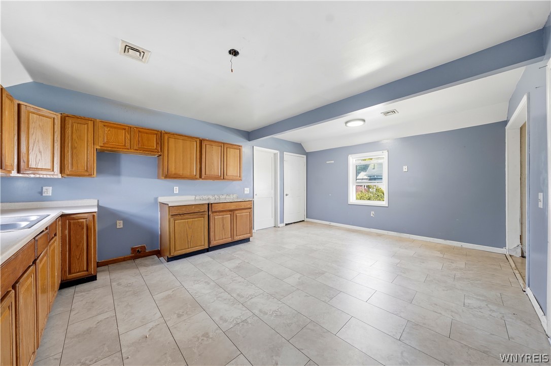 Empty kitchen with honey-colored cabinets, blue-gray walls, and light tile flooring.