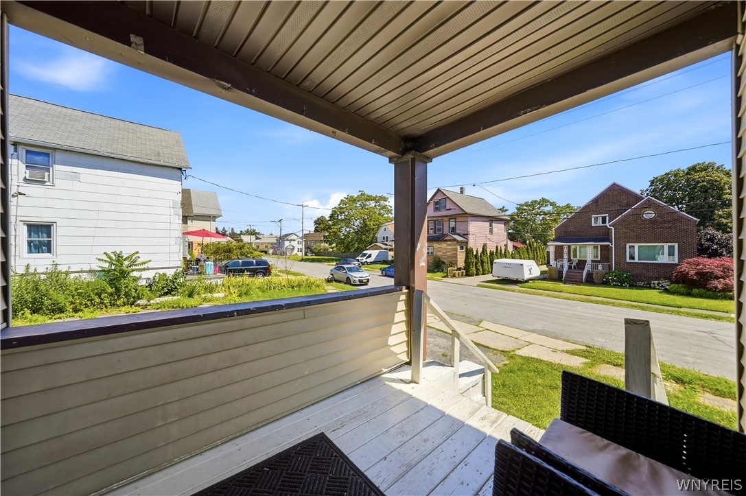 Covered porch with white decking and wicker seating overlooking a residential street.