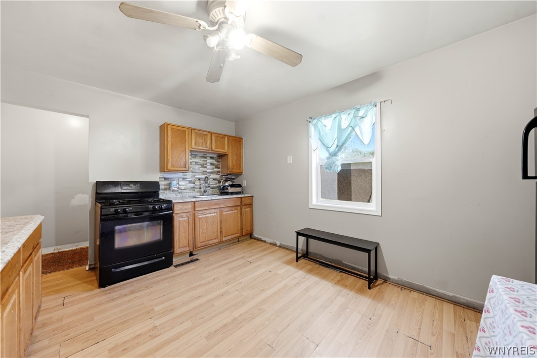 Kitchen with wood cabinets, black range, tiled backsplash, and blue curtains.
