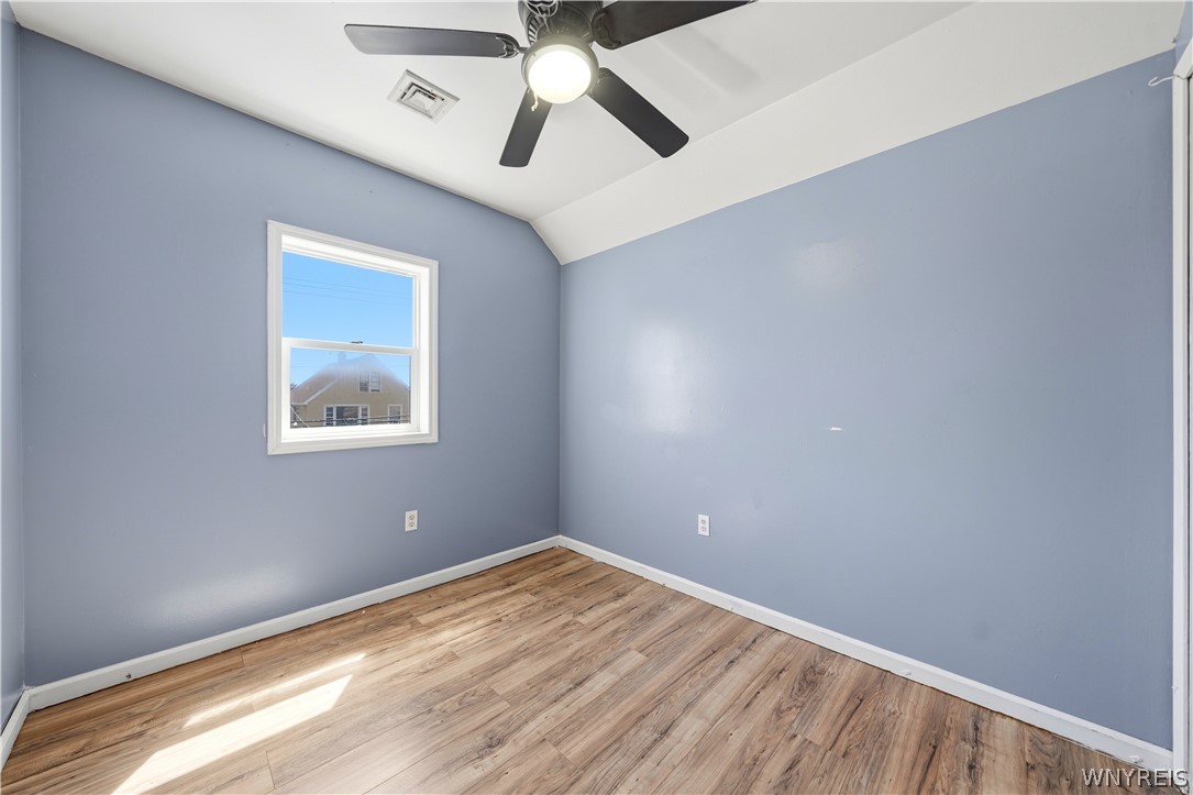 Empty room with blue-gray walls, wood-look flooring, a window, and a ceiling fan with light.
