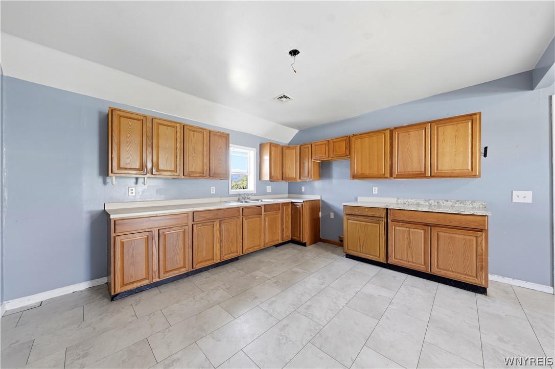 Empty kitchen with honey-colored cabinets, blue walls, and large gray tile flooring.
