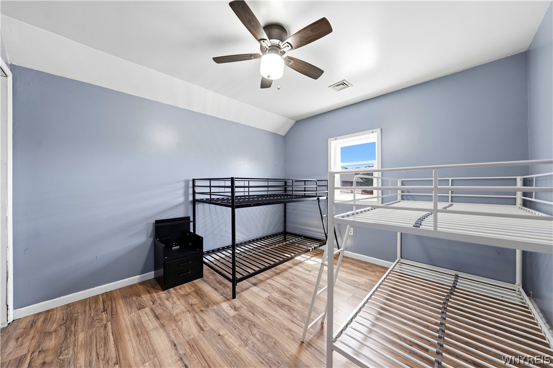 Bedroom with blue walls, two metal bunk bed frames, wood-look flooring, and a ceiling fan.
