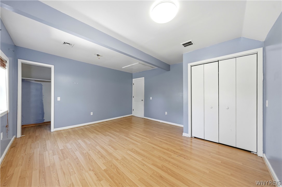 Empty bedroom with light wood floors, blue-gray walls, and a large white folding-door closet.