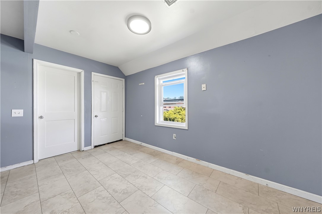 Vacant room with gray walls, tiled floor, two white doors, and a window overlooking greenery.