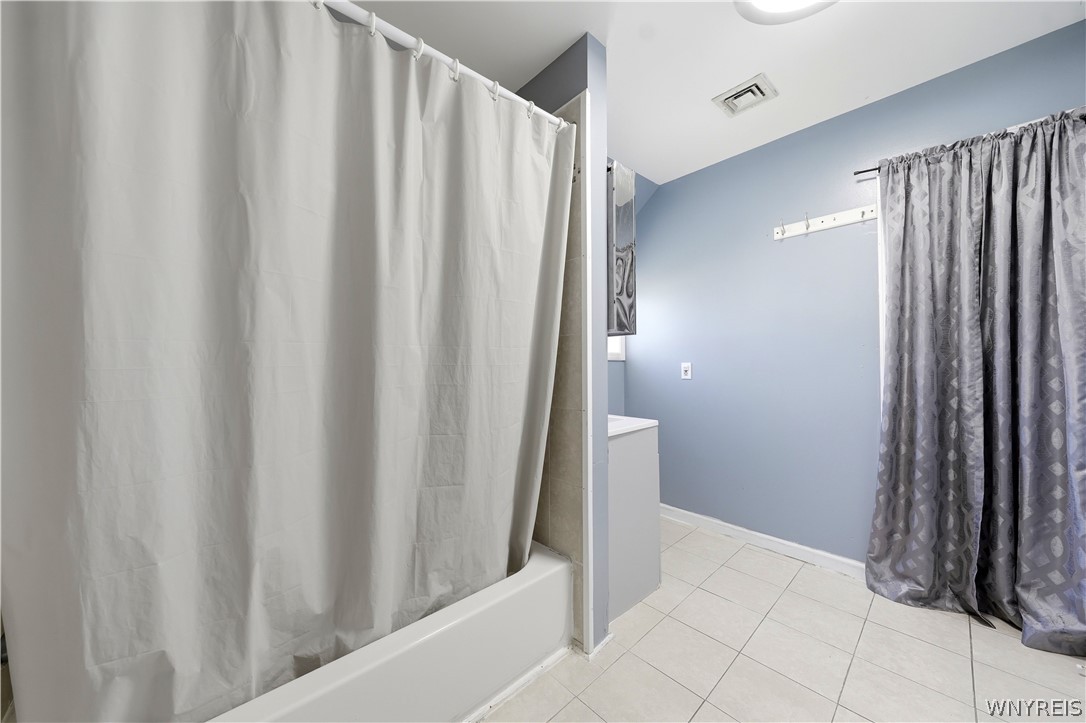 Bathroom with a white bathtub, blue walls, tiled floor, and gray window curtains.