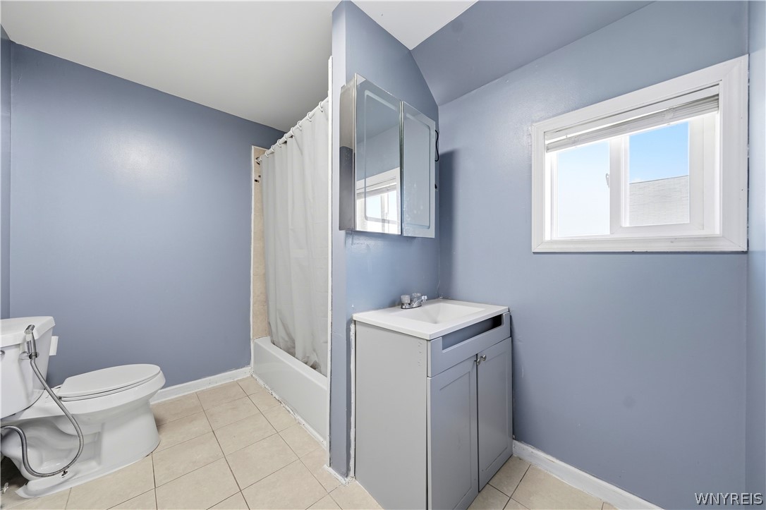 Bathroom with blue-gray walls, a white tub and shower curtain, and a gray vanity beneath a mirrored cabinet.