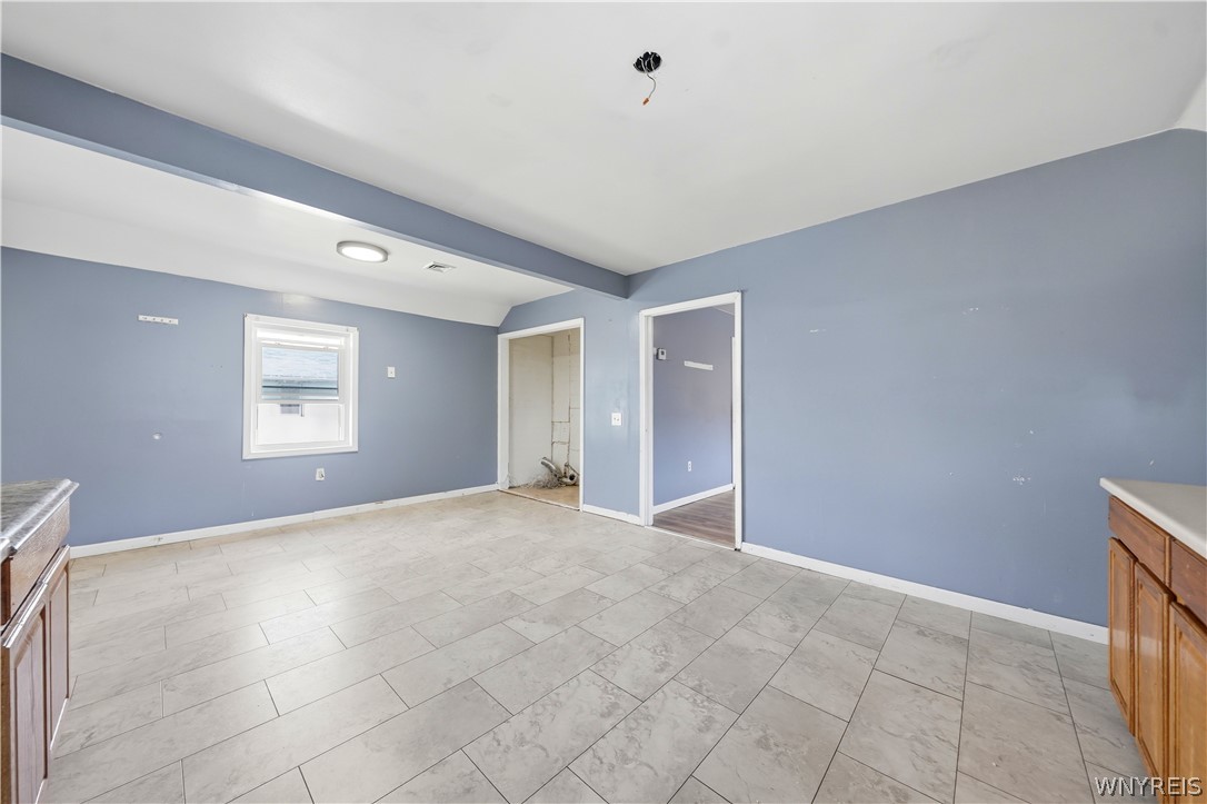 Empty kitchen with blue-gray walls, large tile flooring, and partial wooden cabinets.