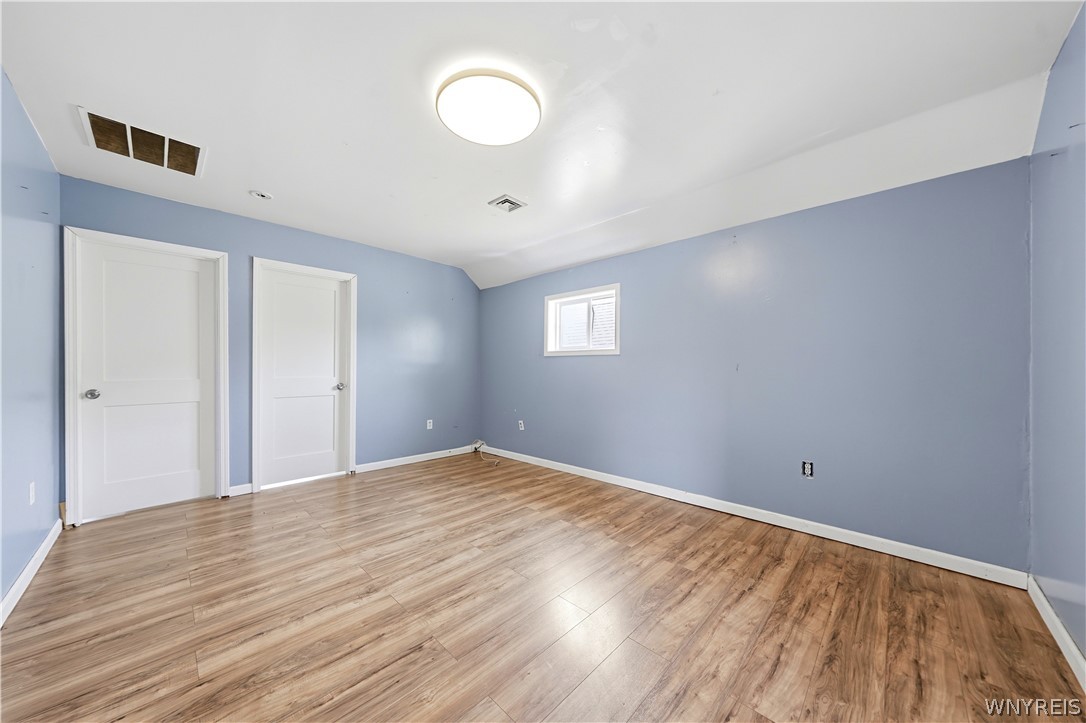 Empty room with blue walls, wood-look flooring, two white doors, and a small shuttered window.