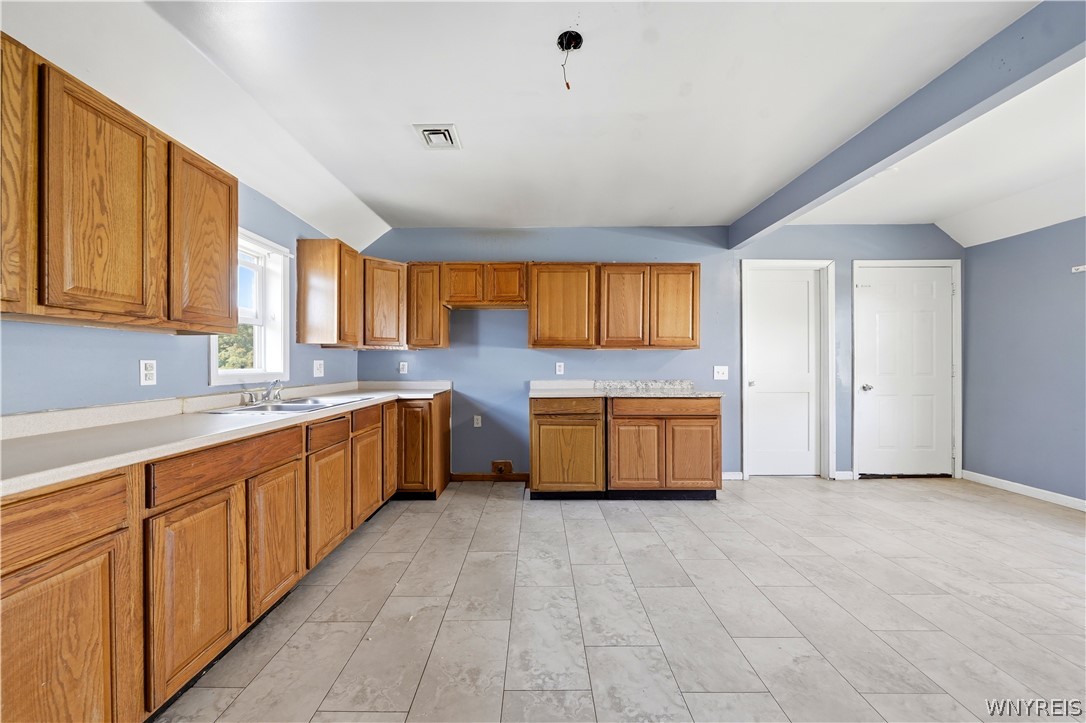 Vacant kitchen with honey-colored cabinets, blue walls, and a sink beneath a window.