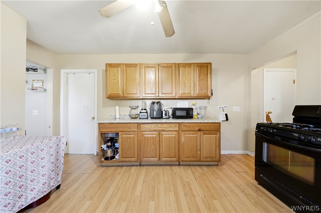 Kitchen with oak cabinets, countertop appliances, a black range, and light wood flooring.