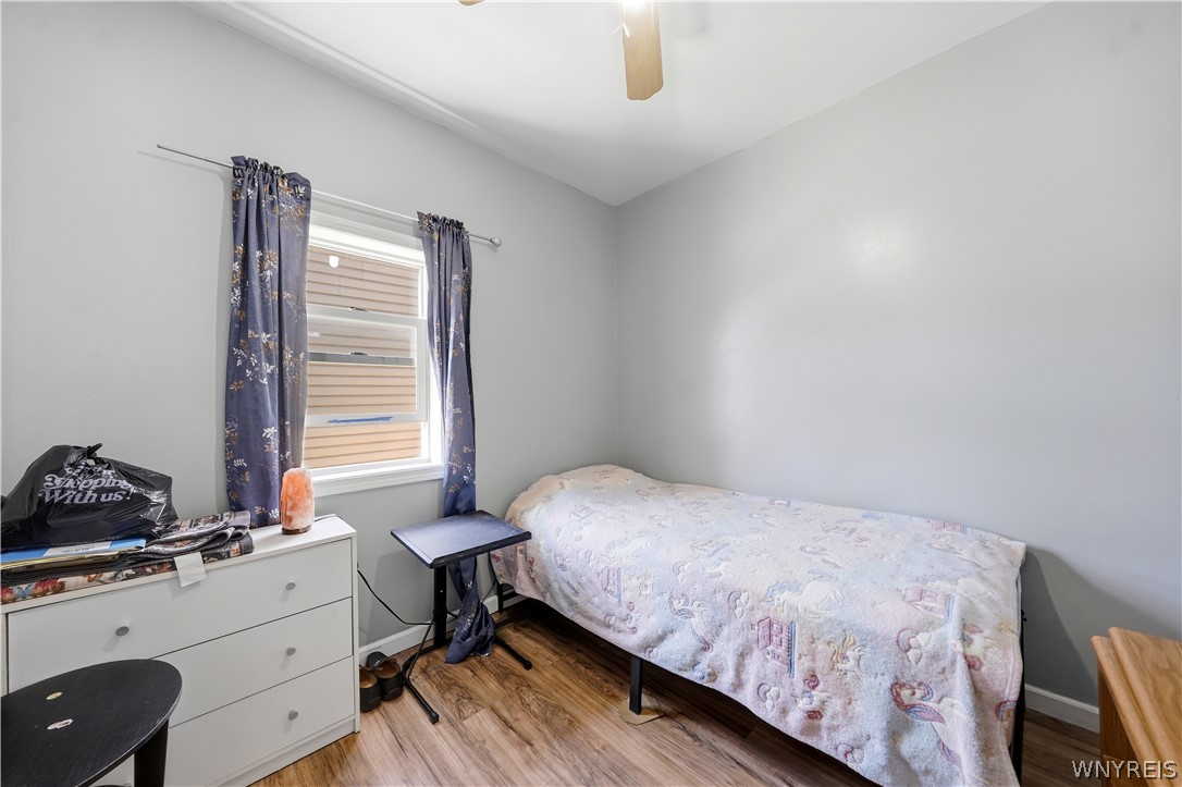 Bedroom with a single bed, blue floral curtains, white dresser, and wood-look flooring.