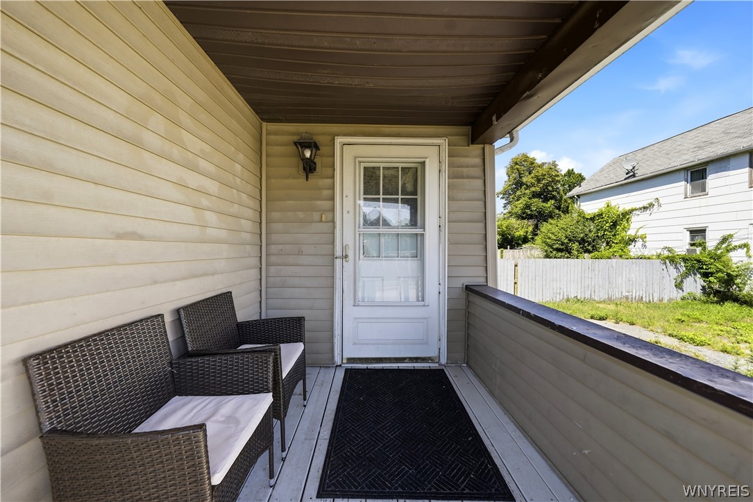 Covered porch with wicker seating, a white storm door, and a view of the fenced yard.
