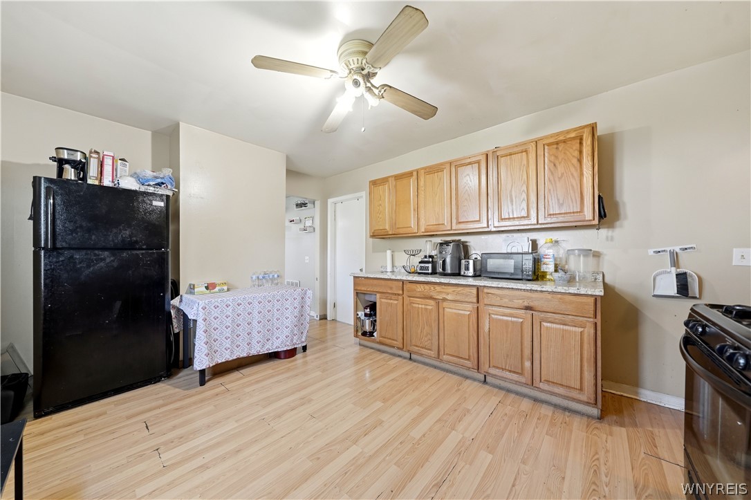 Kitchen with wood cabinets, a black refrigerator, and light wood flooring.