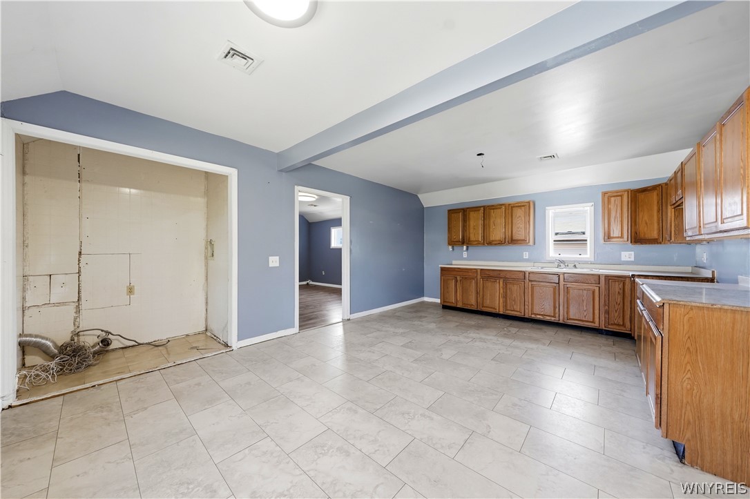 Vacant kitchen with wood cabinets, tiled floors, and an exposed utility alcove.