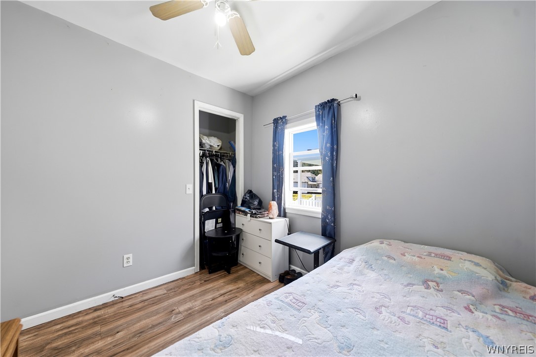 Bedroom with gray walls, a patterned bedspread, an open closet, and blue curtains framing the window.