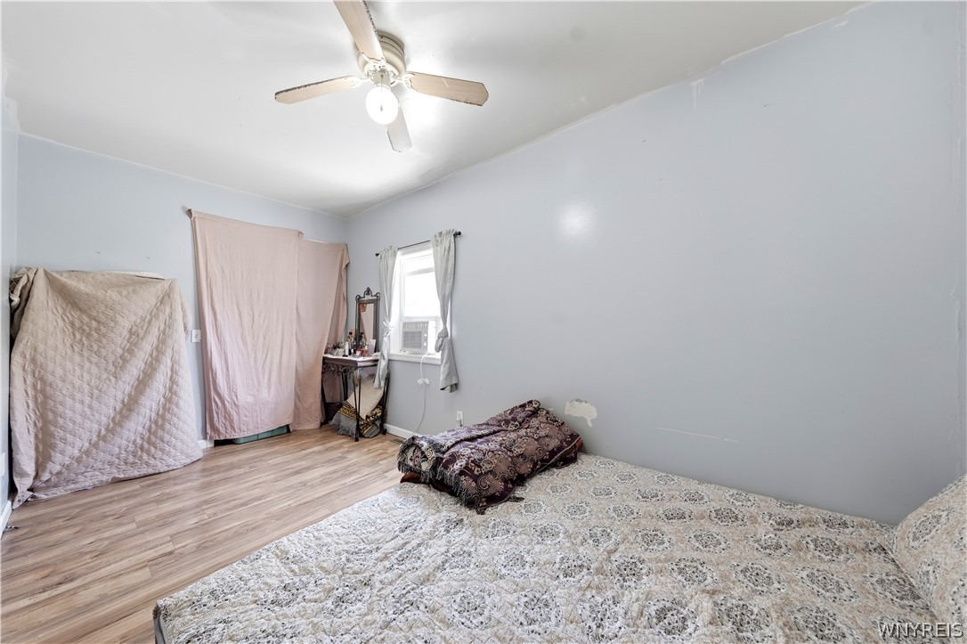 Bedroom with a patterned bedspread, covered furniture, a small vanity, and a window air conditioner.