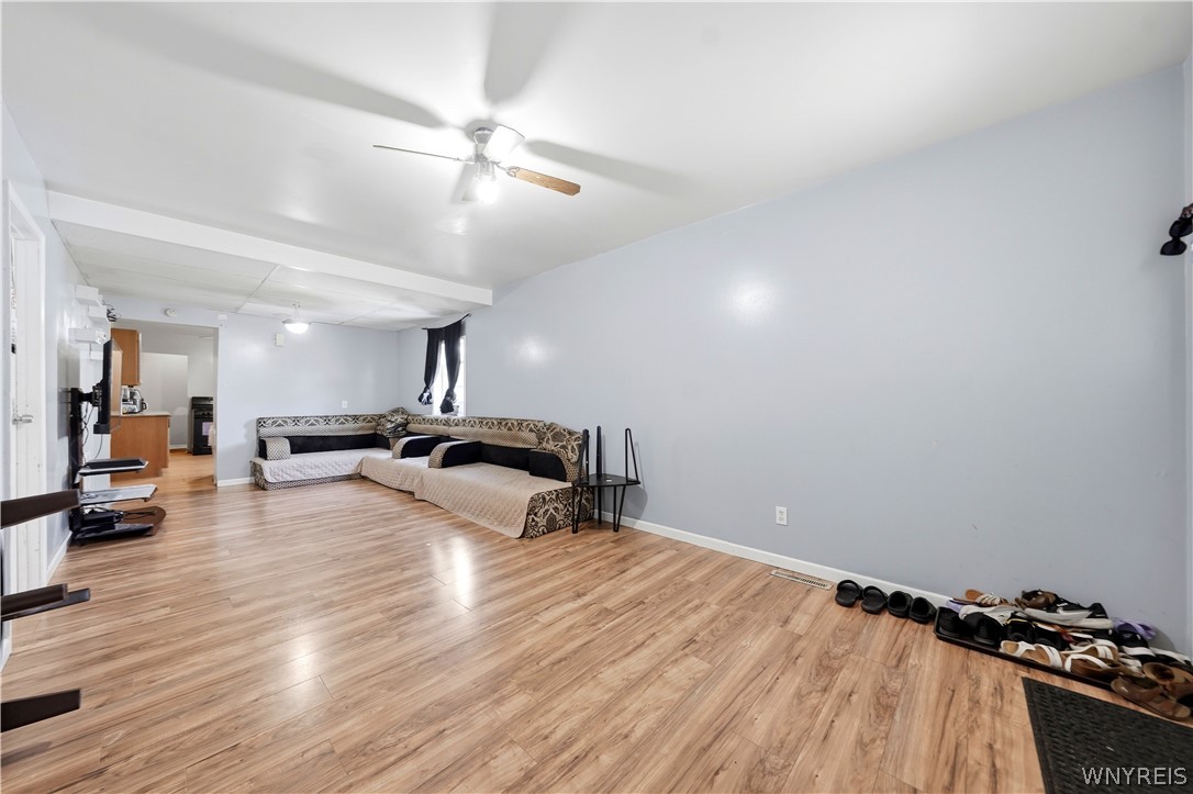 Living room with a patterned sectional, light wood flooring, and a ceiling fan.