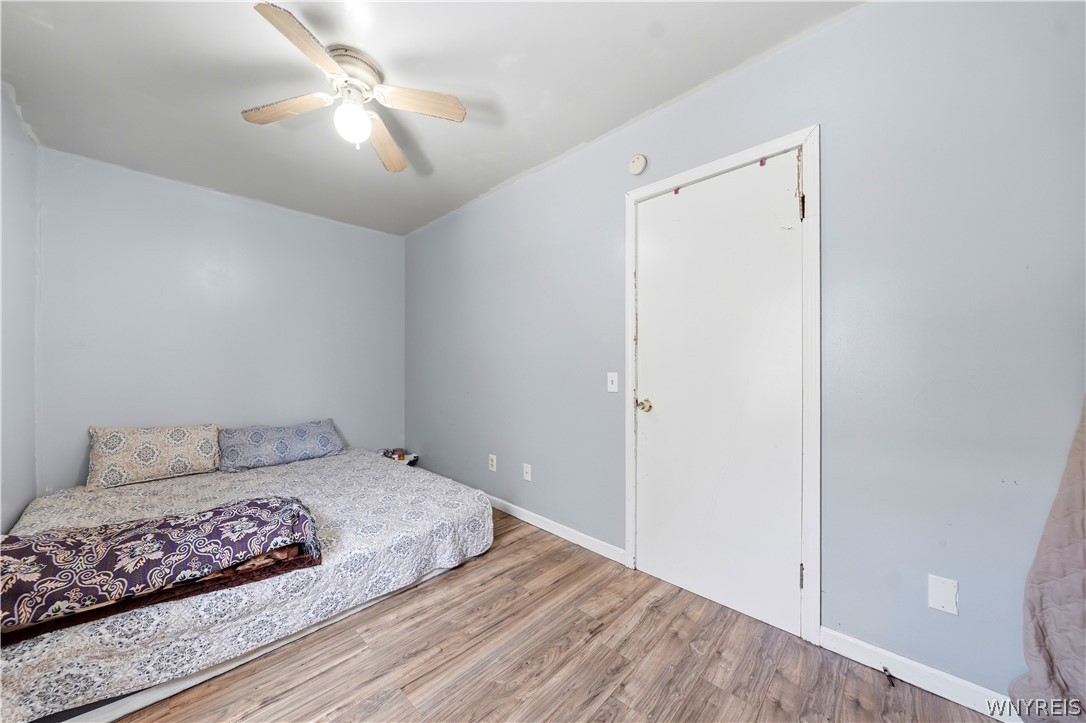 Bedroom with patterned bedding, wood-look flooring, and a ceiling fan above the bed.