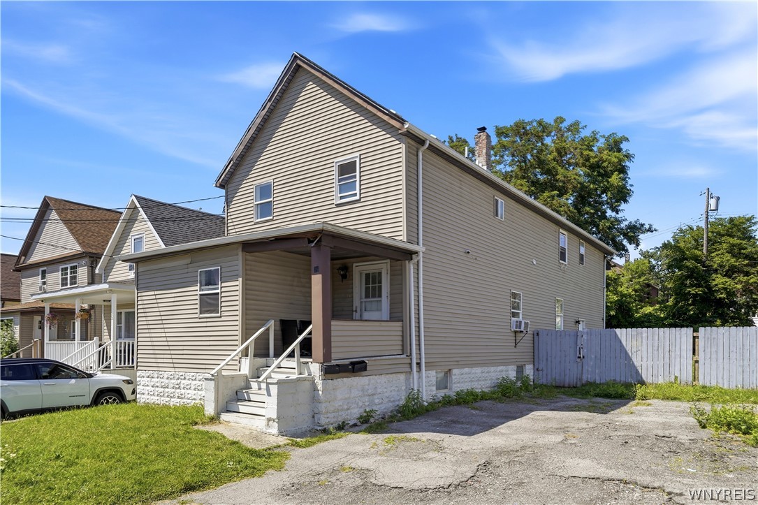 Two-story beige-sided house with a covered porch, white fence, and cracked driveway.