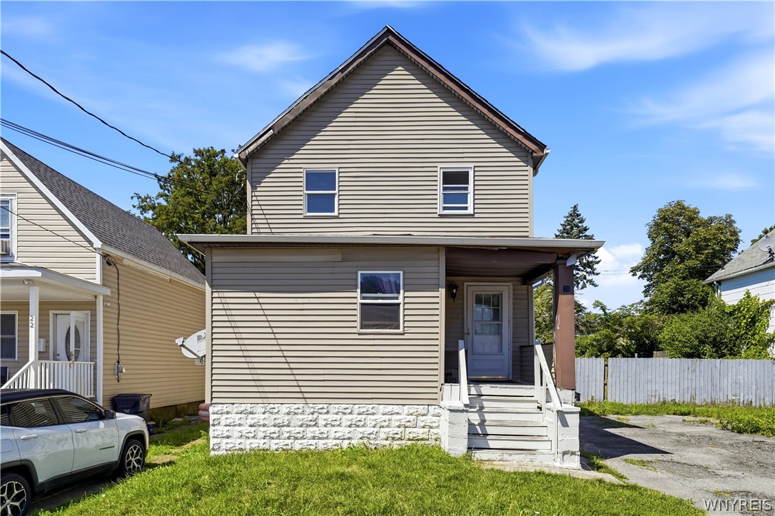 Two-story beige house with a covered porch, white steps, and a small front lawn.