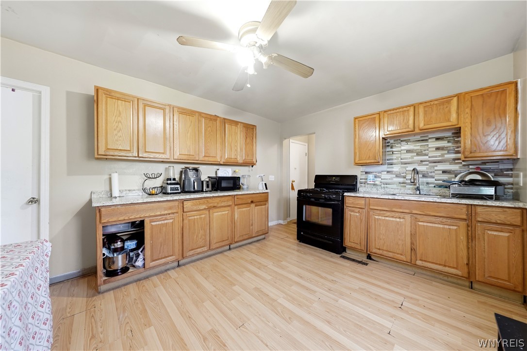 Kitchen with honey-colored cabinets, light wood flooring, and a black gas range beneath a striped tile backsplash.