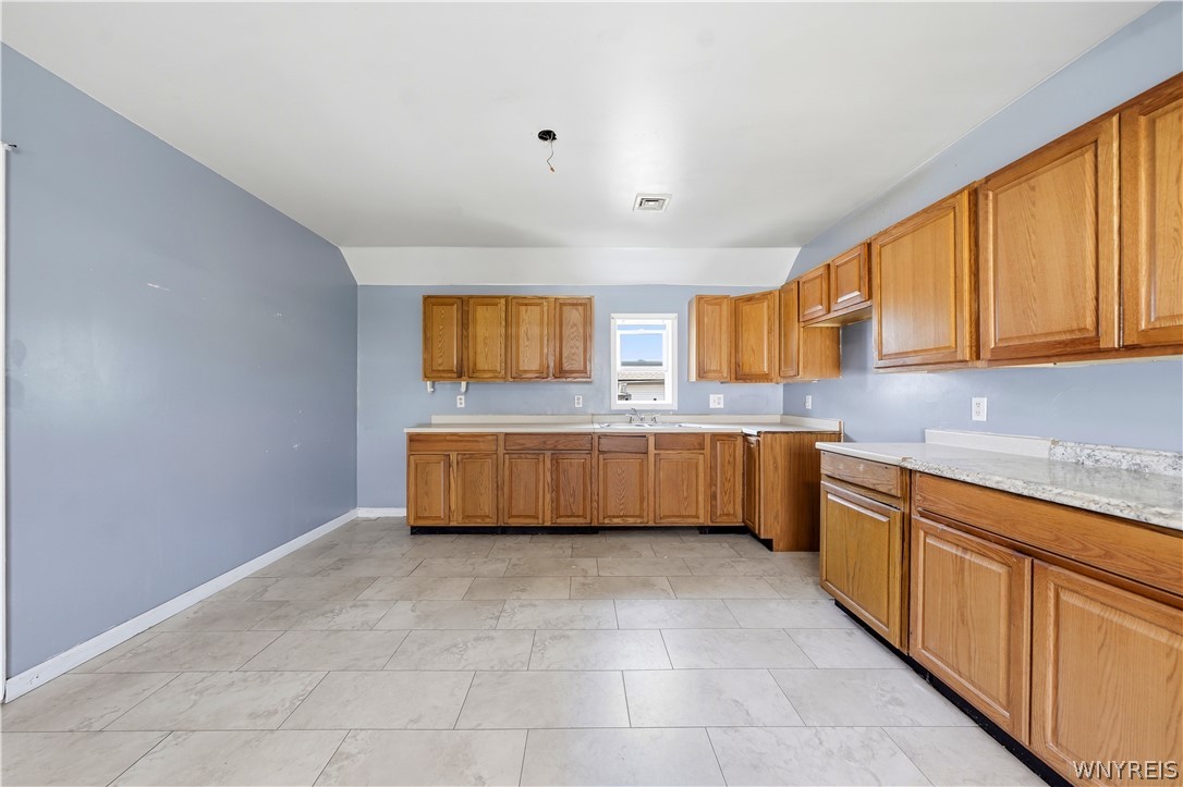Empty kitchen with extensive wood cabinetry, stone counters, and gray tile floors.