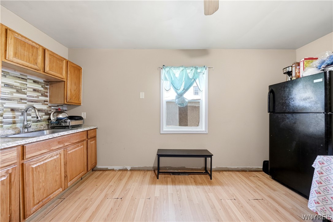 Kitchen with wood cabinets, tiled backsplash, and a black refrigerator beside a curtained window.