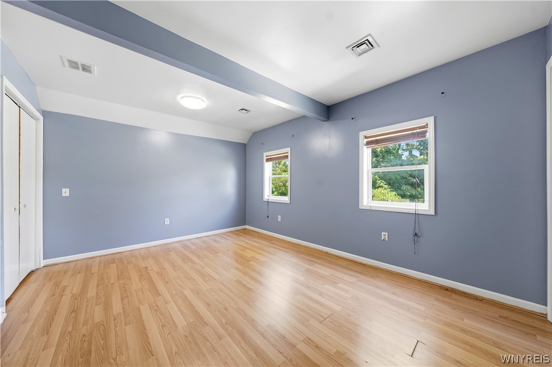 Vacant room with blue-gray walls, light wood floors, and two windows with blinds.