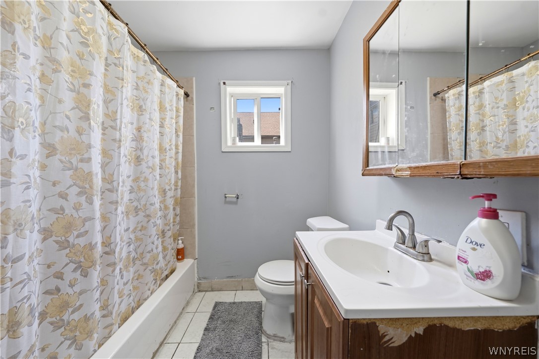 Bathroom with a floral shower curtain, wood vanity, mirrored cabinet, and small window.