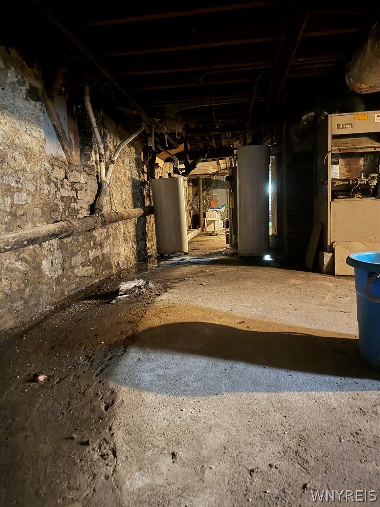 Unfinished basement with exposed stone walls, utility tanks, and a furnace.