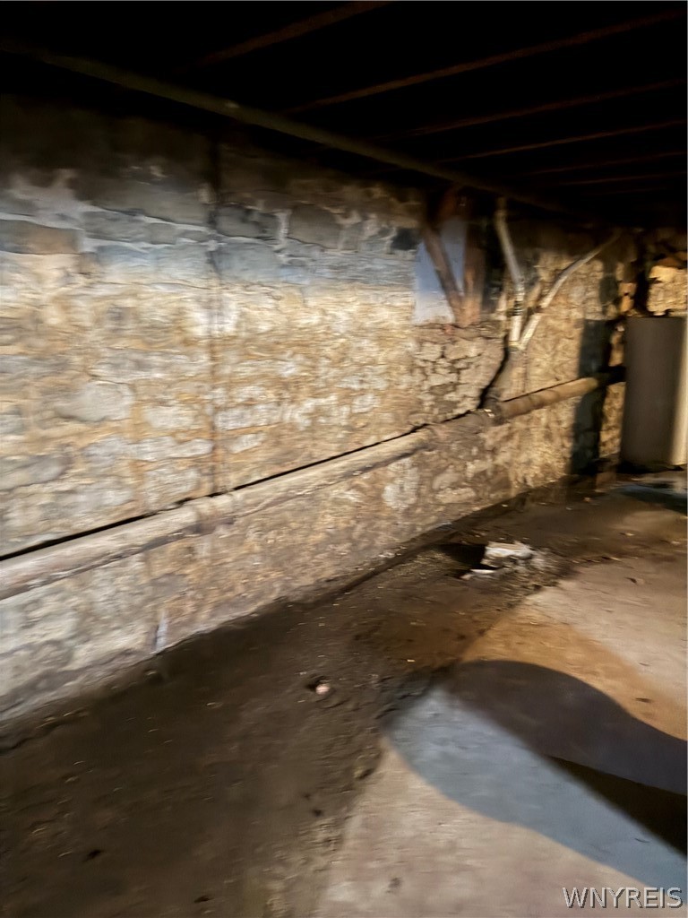Unfinished basement with rough stone foundation walls, exposed joists, pipes, and damp concrete floor.